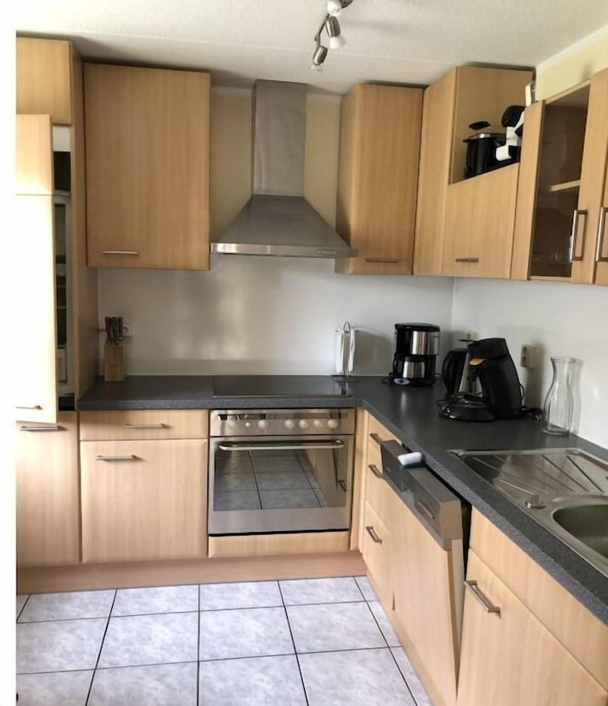 A compact kitchen with wooden cabinets, a stainless steel range hood, a built-in oven, and a black countertop.