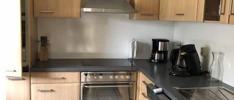 Una cocina compacta con gabinetes de madera, extractor de acero inoxidable, horno empotrado y encimera negra.