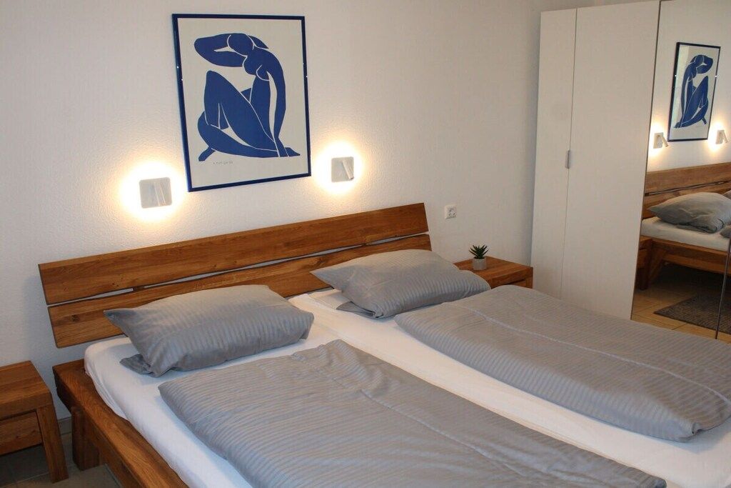 Una cama doble con cabecera de madera, dos mesitas de noche y un aplique de pared.