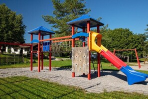 A playground with a slide, climbing structures, and a covered play area. - Holiday home "Breitenberg" (Lechbruck)