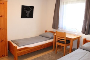 A small, single-bed room with a wooden desk and chair, a bedside table with a lamp, and a framed deer head artwork on the wall. - Holiday home "Breitenberg" (Lechbruck)