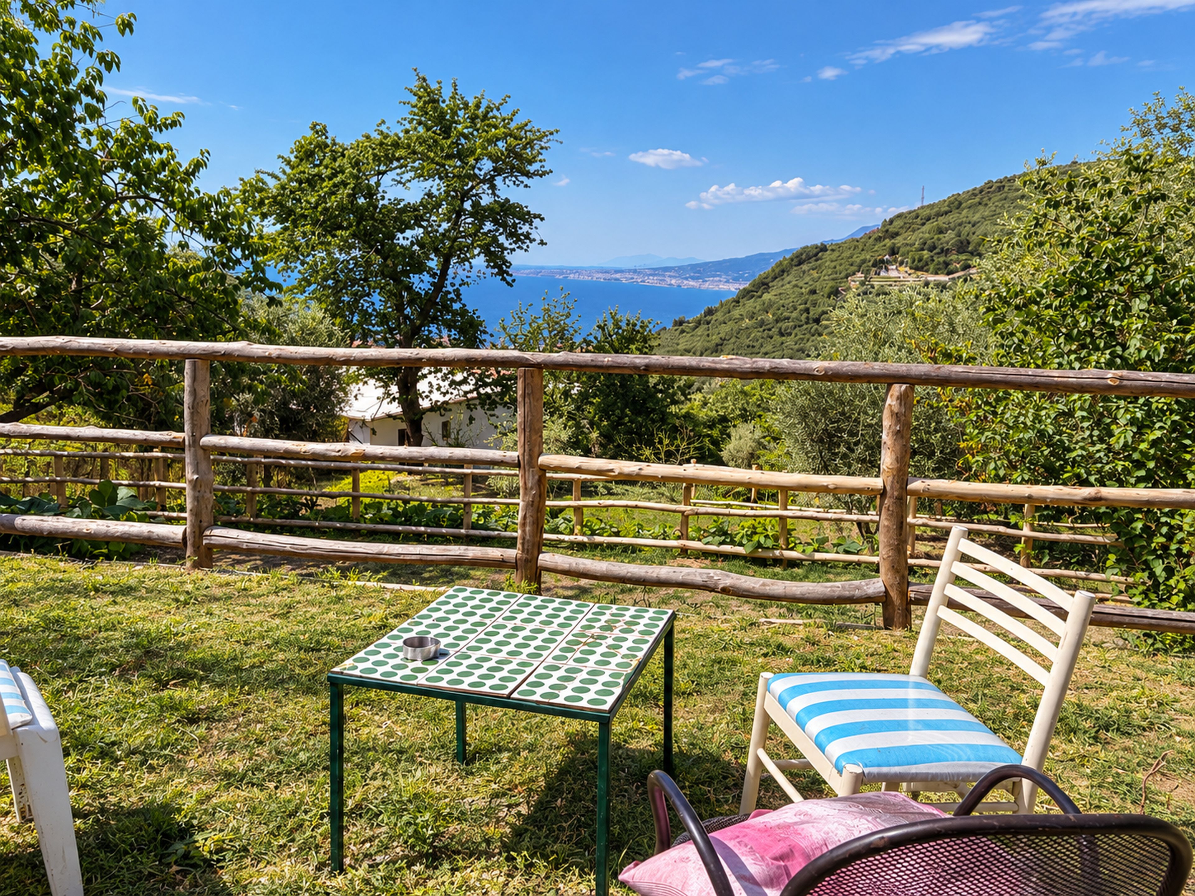 Ein Tisch mit Stuhl auf einer grünen Wiese mit Blick auf das Meer und die Hügel.