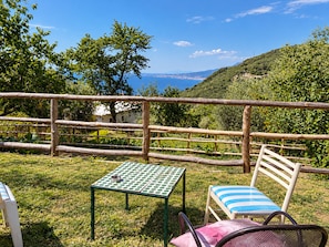 A table and chair set on a grassy lawn with a view of the sea and hills. - Ara Solis (AROLA-PREAZZANO)