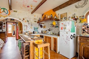 A kitchen with a wooden table, bar stools, a refrigerator, and various kitchen utensils. - Ara Solis (AROLA-PREAZZANO)