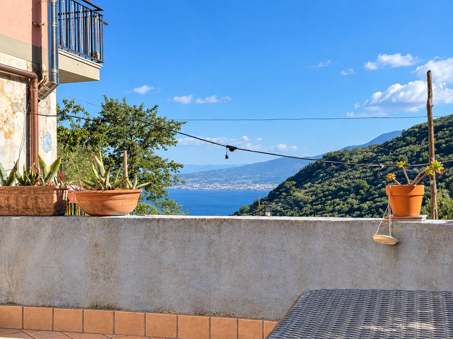 A balcony with potted plants, a view of a coastal landscape, and a clear sky.