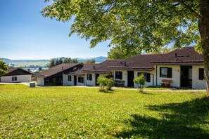 A row of houses with a grassy lawn in front, a clear sky, and distant hills. - Holiday home in Allgäu with 2 bedrooms (Lechbruck)