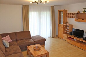 A living room with a brown sofa, a wooden coffee table, and a TV stand with a flat-screen TV. - Holiday home in Allgäu with 2 bedrooms (Lechbruck)