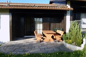 A covered outdoor area with a table and chairs, a stack of wooden pallets, and a small tree. - Holiday home in Allgäu with 2 bedrooms (Lechbruck)