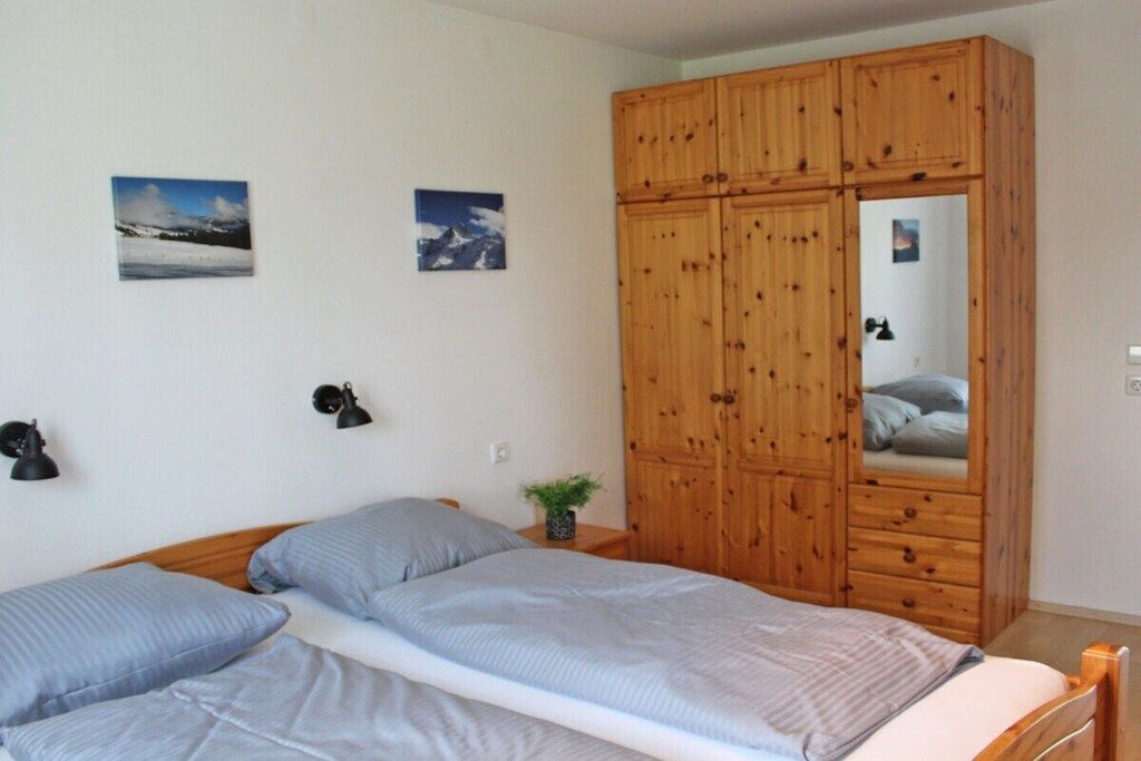 A bedroom with a bed, two wall-mounted lamps, and a wooden wardrobe with a mirror.
