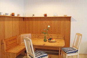 A wooden dining area with a bench and two chairs, a vase with a flower, and a fruit basket on the table. - Holiday home in Allgäu with 2 bedrooms (Lechbruck)