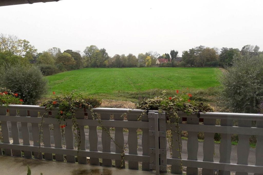 A view of a green field from a balcony with a wooden railing.