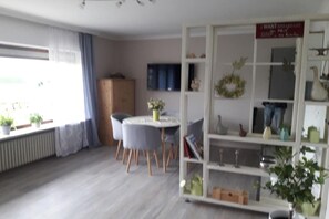 A room with a dining table, chairs, a bookshelf, and a radiator. - Holiday apartment with 1 bedroom (Wurster Nordseeküste)