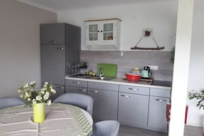 A compact kitchen with grey cabinets, a green chair, and a dining table with a vase of flowers. - Holiday apartment with 1 bedroom (Wurster Nordseeküste)
