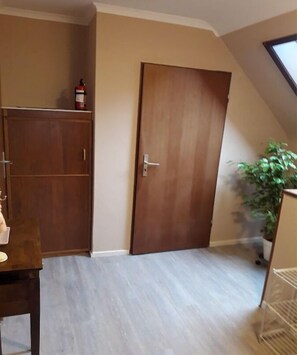 Ein Zimmer mit einem Holzschrank, einer geschlossenen Tür, einem kleinen Tisch mit Stuhl und einer Topfpflanze.