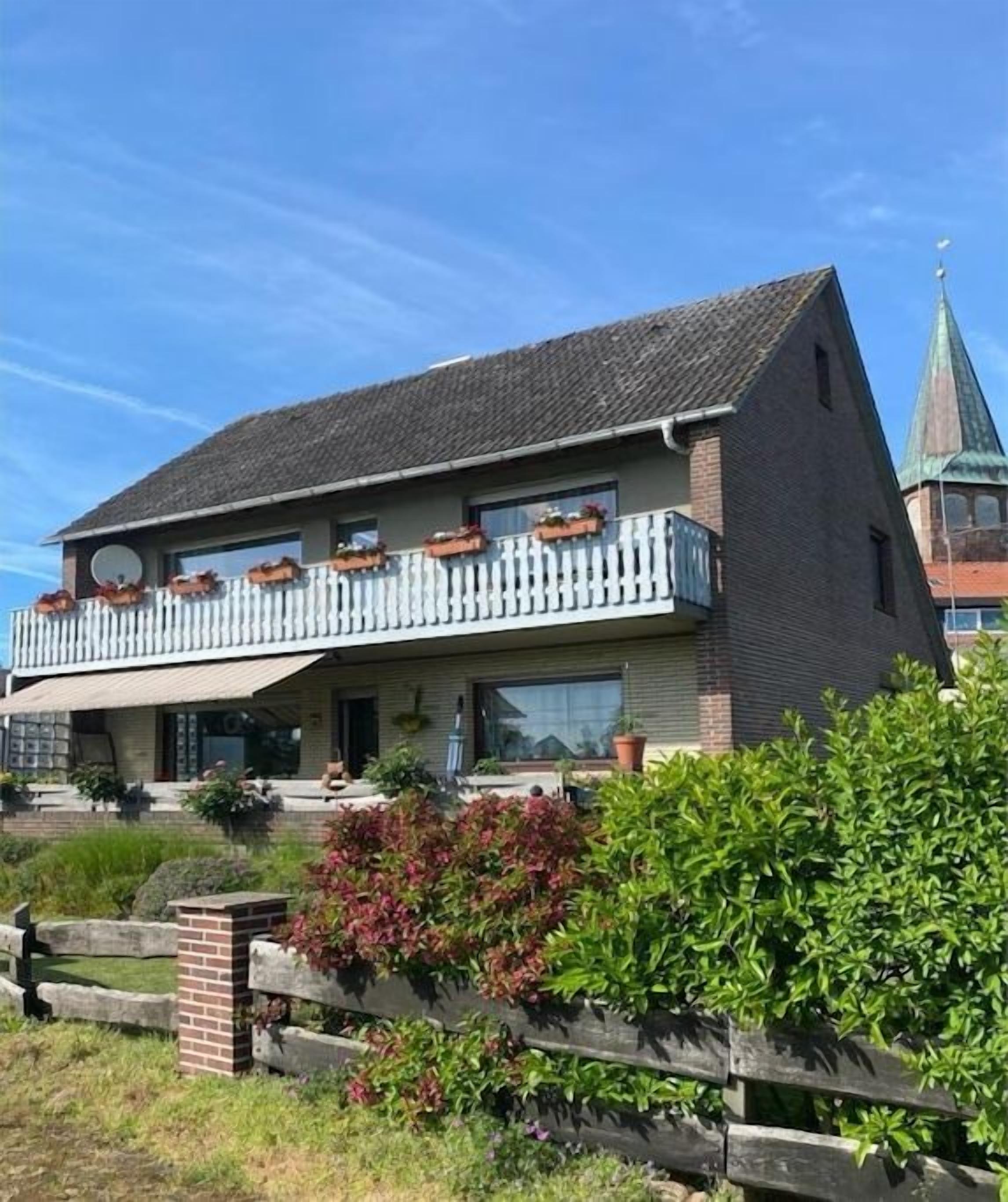 En toetagers bygning med balkon, facade af mursten og en mindre tårnagtig struktur i baggrunden.