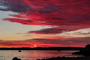Un coucher de soleil sur une étendue d’eau, avec en silhouette une côte rocheuse.