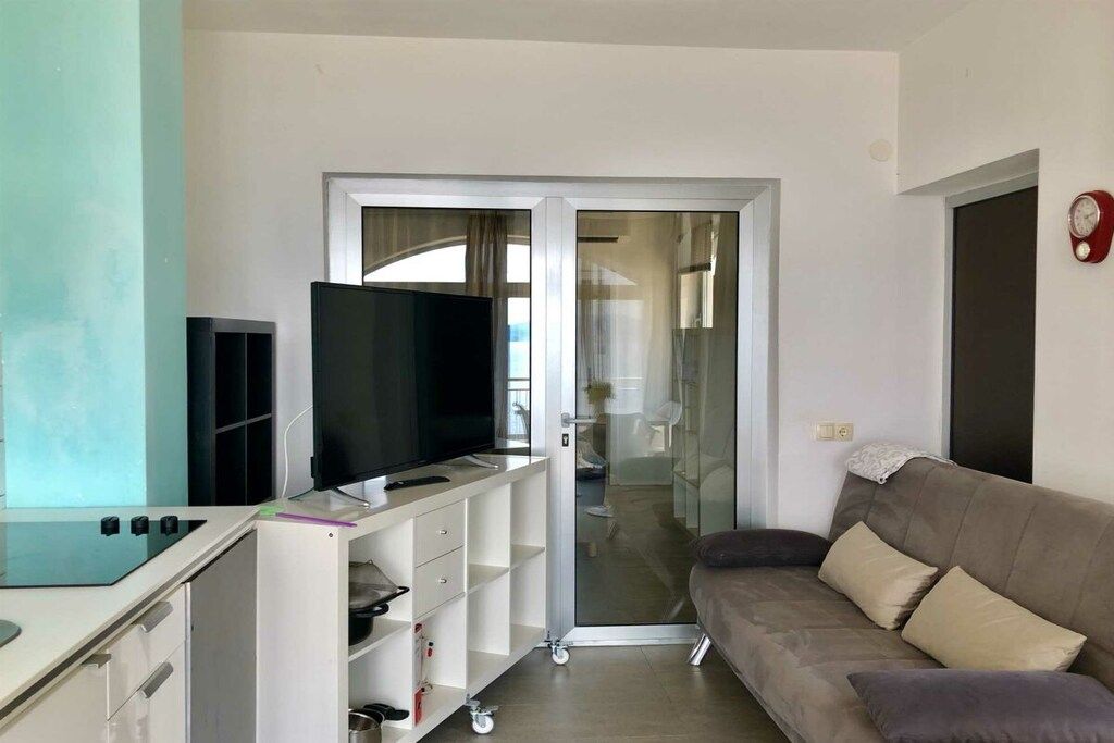 Una sala de estar moderna con un televisor de pantalla plana, un sofá y una puerta corrediza de vidrio que da a un balcón.