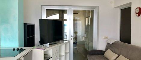 A modern living room with a flat-screen TV, a sofa, and a sliding glass door leading to a balcony.