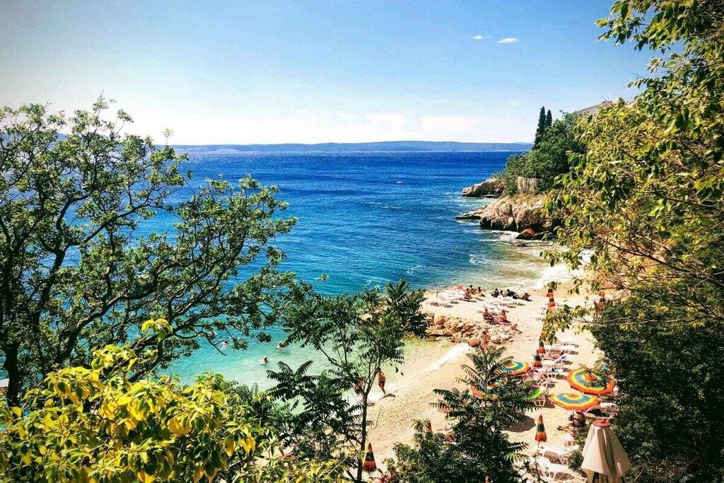 Une plage bordée d’une eau d’un bleu limpide, entourée de verdure et de falaises rocheuses.