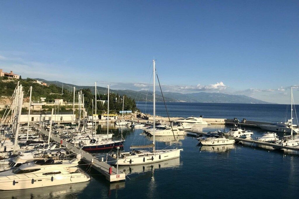 Un puerto deportivo con varias embarcaciones amarradas, cielo despejado y un paisaje montañoso al fondo.