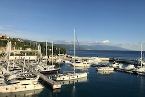 Ein Yachthafen mit mehreren vertäuten Booten, bewölktem Himmel und hügeliger Landschaft im Hintergrund.