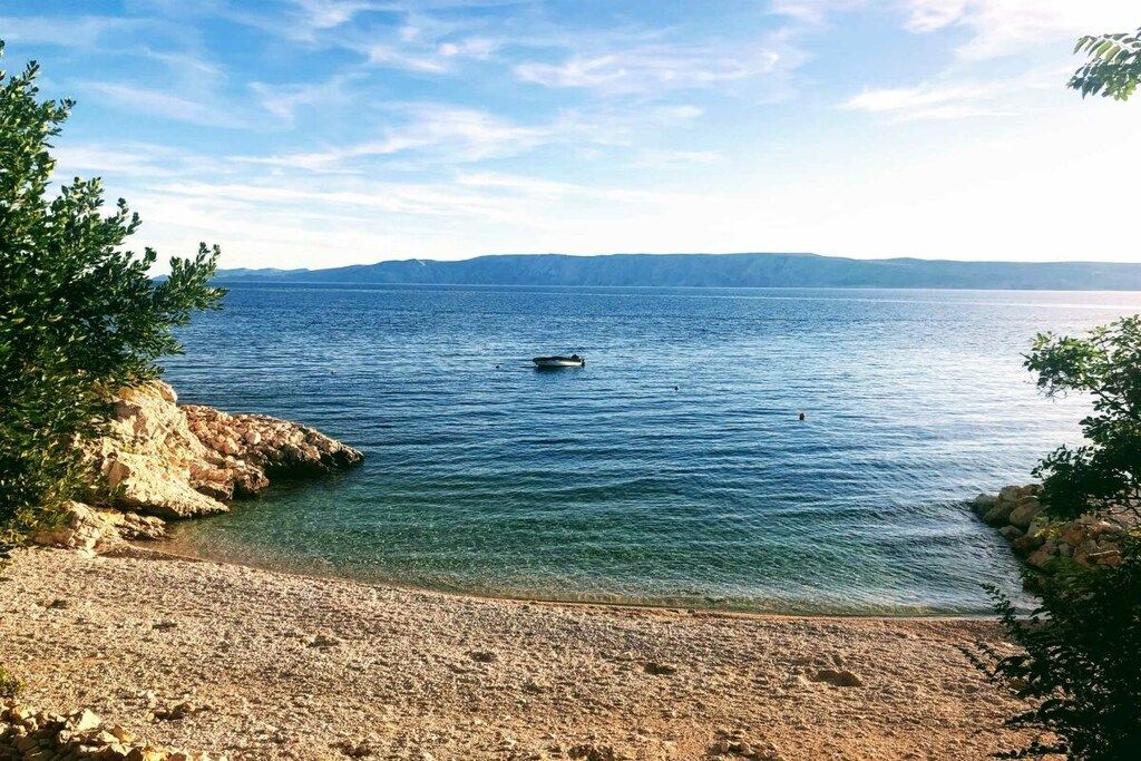 Une plage à l’eau claire, un rivage rocheux et des montagnes qui se dessinent à l’horizon.