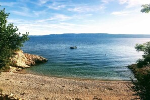 Ein Strand mit klarem Wasser, felsigem Ufer und Bergen im Hintergrund.