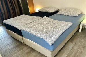 Ein Doppelbett mit gemusterten Betttextilien, ein Nachttisch und ein Vorhang.