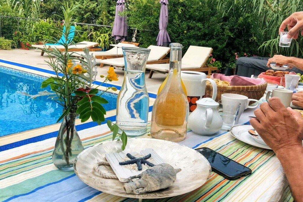 Un área de comedor junto a la piscina con sillones reclinables, una mesa dispuesta con platos, vasos y una botella.