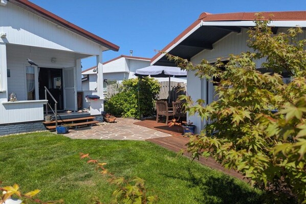 A row of white mobile homes with a paved patio area and a small garden.