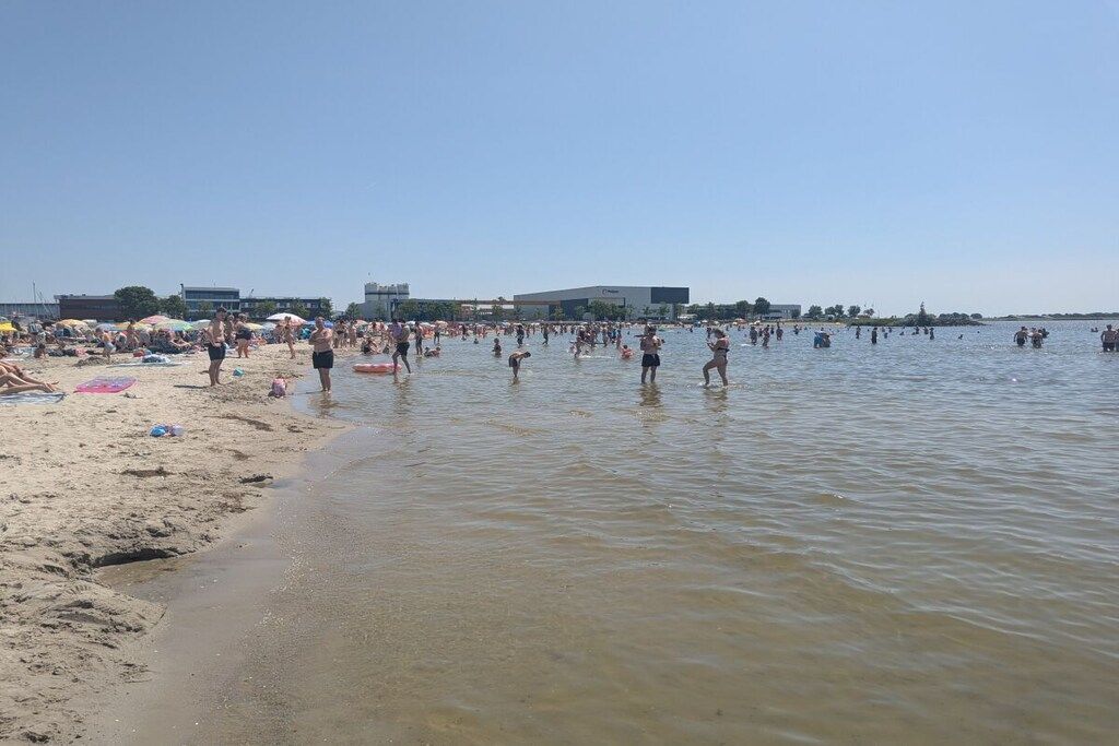 Una platja plena de gent a l'aigua i a la sorra.