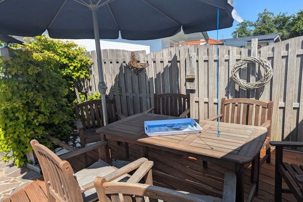 An outdoor wooden deck with a table and chairs, surrounded by a wooden fence, and a butterfly resting on the fence.