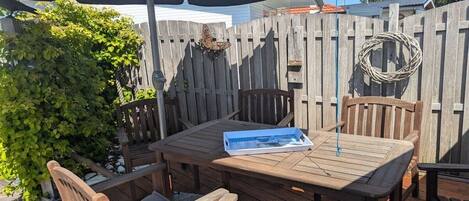 An outdoor wooden deck with a table and chairs, surrounded by a wooden fence, and a butterfly resting on the fence.