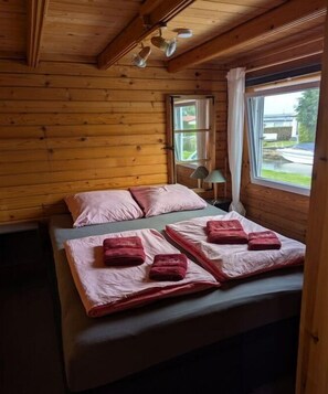 A wooden cabin room with a bed, pillows, and a window with curtains.