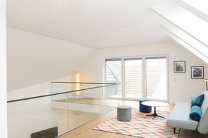 A modern interior with a glass staircase, a sofa with cushions, a patterned rug, and a large window with a view. - Holiday home with 3 bedrooms (Schliengen)