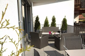 Ein Balkon mit Korbmöbeln, einem Tisch mit Blumen in einer Vase und Kübelpflanzen.