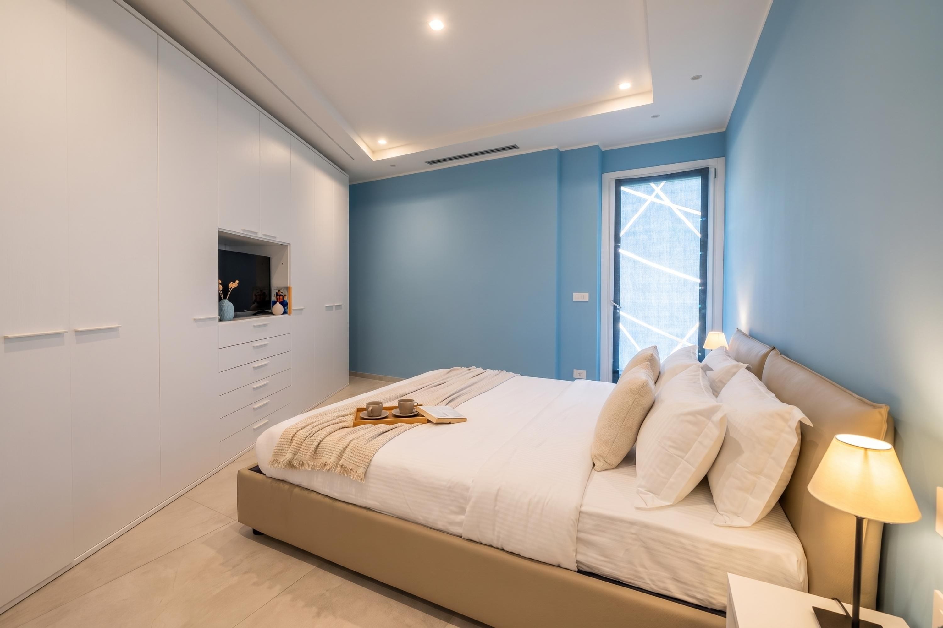A modern bedroom with a large bed, a nightstand, a bedside lamp, and a window with a view.