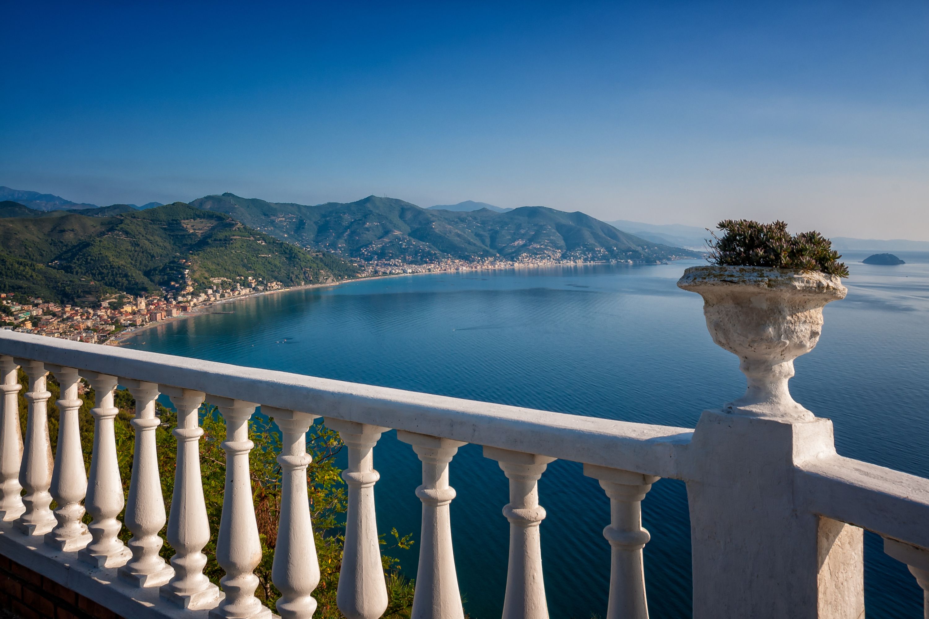 A balcony with a view of a coastal town and mountains.