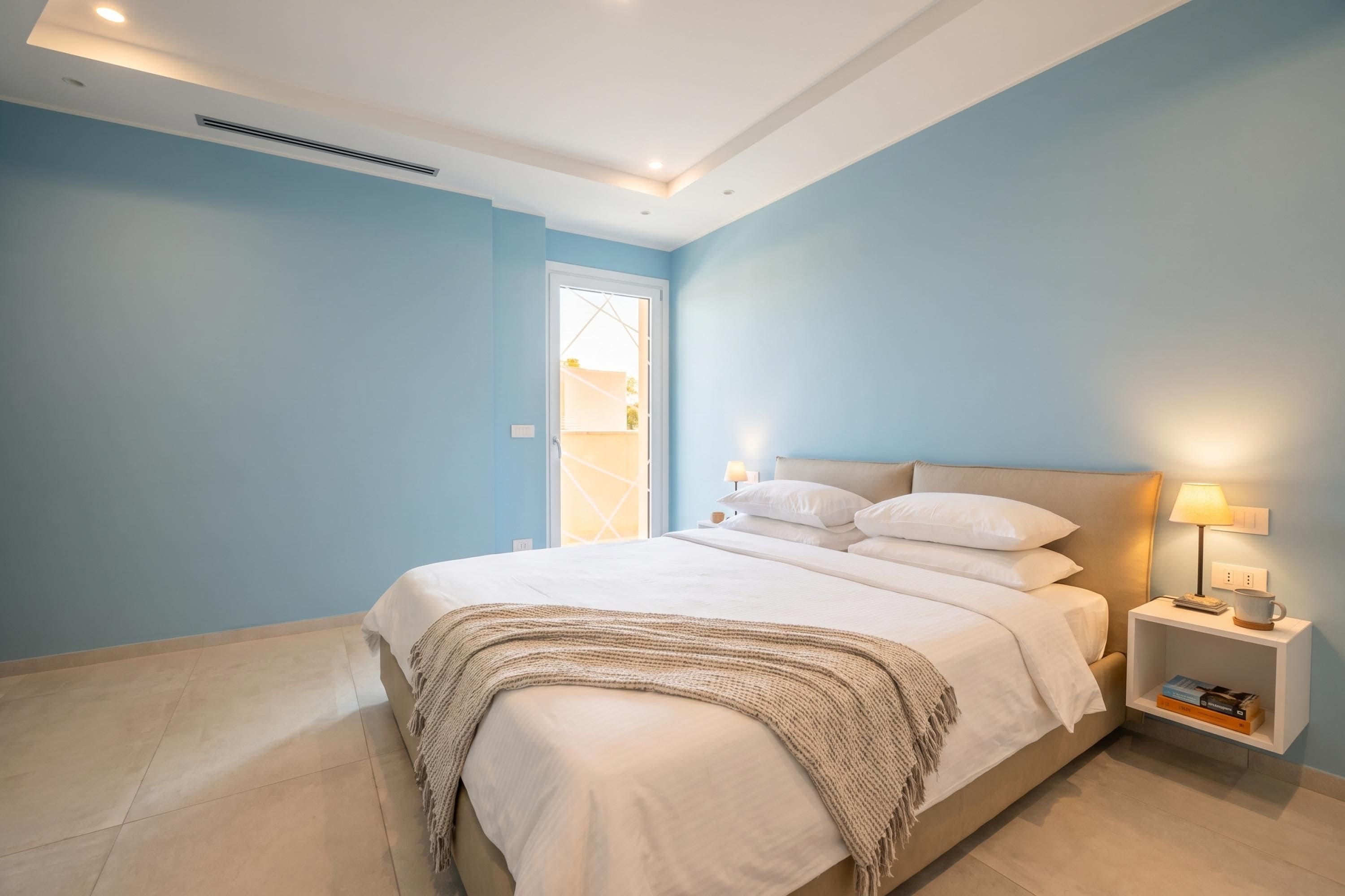 Un dormitorio con cama, mesitas de noche, lámpara y una puerta.