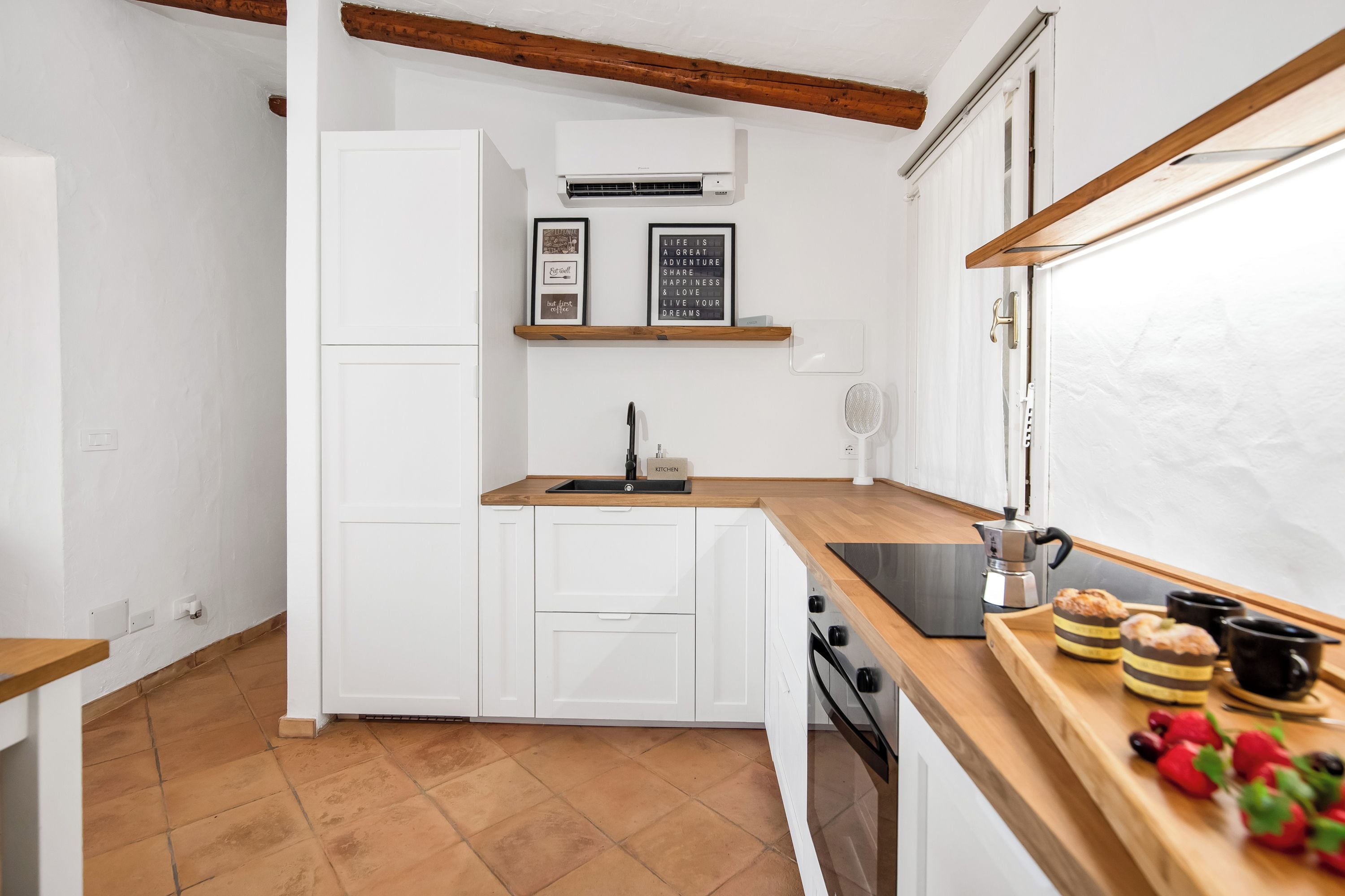 Cozinha compacta com armários brancos, bancada de madeira, forno embutido e ar-condicionado fixado na parede.