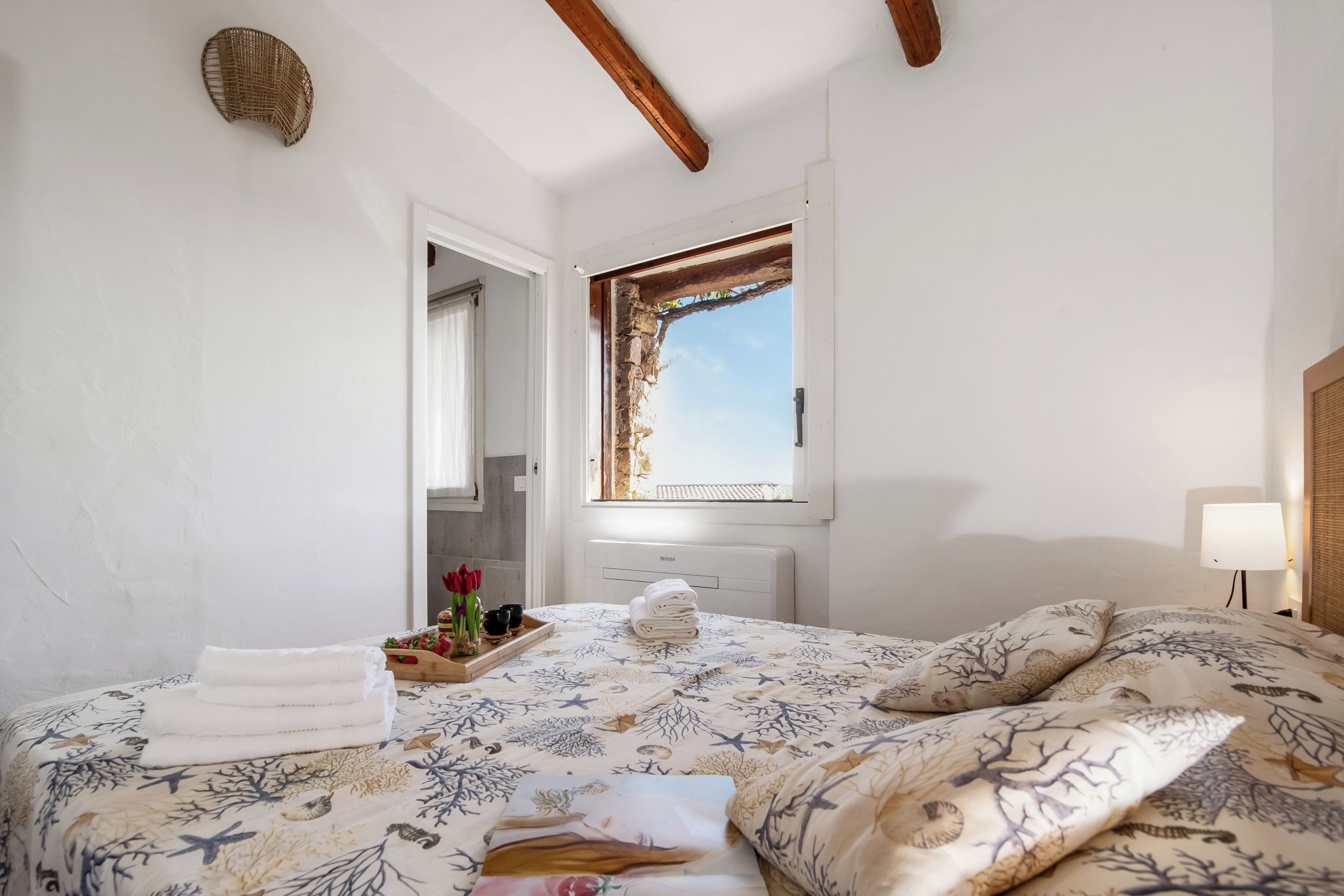 Une chambre à coucher comprenant un lit, une fenêtre, une table de chevet avec des serviettes, une lampe et une étagère fixée au mur.