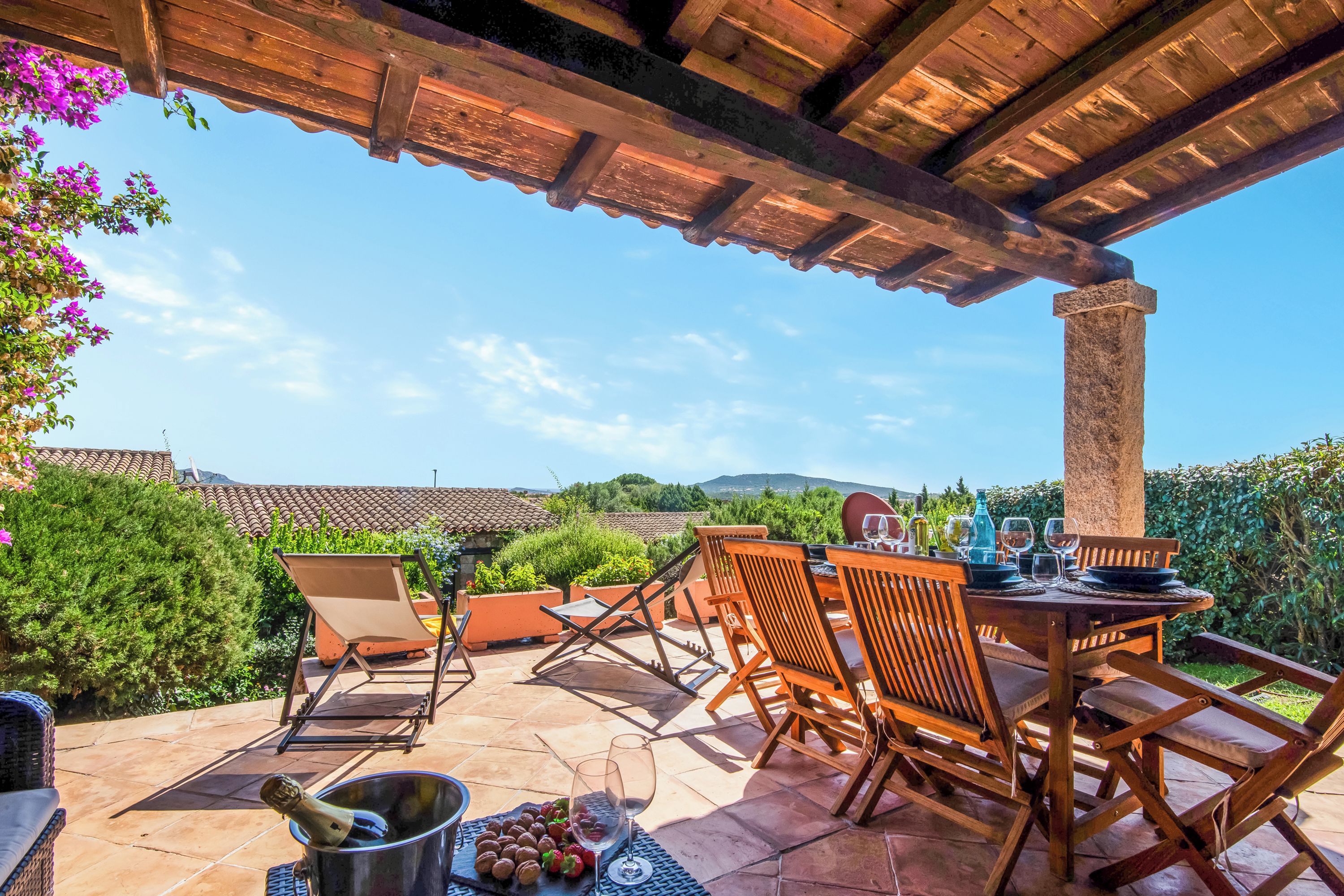 An outdoor patio with wooden furniture, a table set for dining, and a view of the countryside.