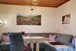 A cozy living room with a sofa, a dining table with chairs, a chandelier, and wall art. - Holzner-Hof "Hochgern" (Marquartstein)