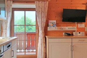 A kitchen with a window, a flat-screen TV mounted above the counter, and a balcony with a railing. - Holzner-Hof "Hochgern" (Marquartstein)
