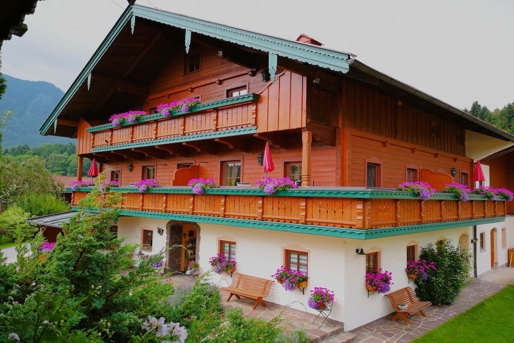A wooden chalet with balconies, flower boxes, and a stone pathway.