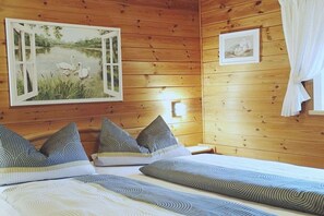 A wooden-paneled room with a bed, pillows, a framed picture of swans, and a bedside lamp. - Holzner-Hof "Hochgern" (Marquartstein)