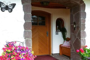 A wooden door with a herringbone pattern, a stone archway, and a bench with a checkered cushion. - Holzner-Hof "Hochgern" (Marquartstein)