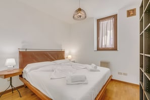 Ein ordentlich bezogenes Bett mit weißen Leinen, eine Nachttischlampe und eine Pendelleuchte.