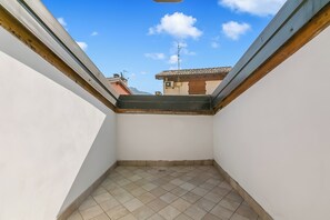 Ein schmaler Balkon mit Fliesenboden, weißen Wänden und Blick auf angrenzende Gebäude.