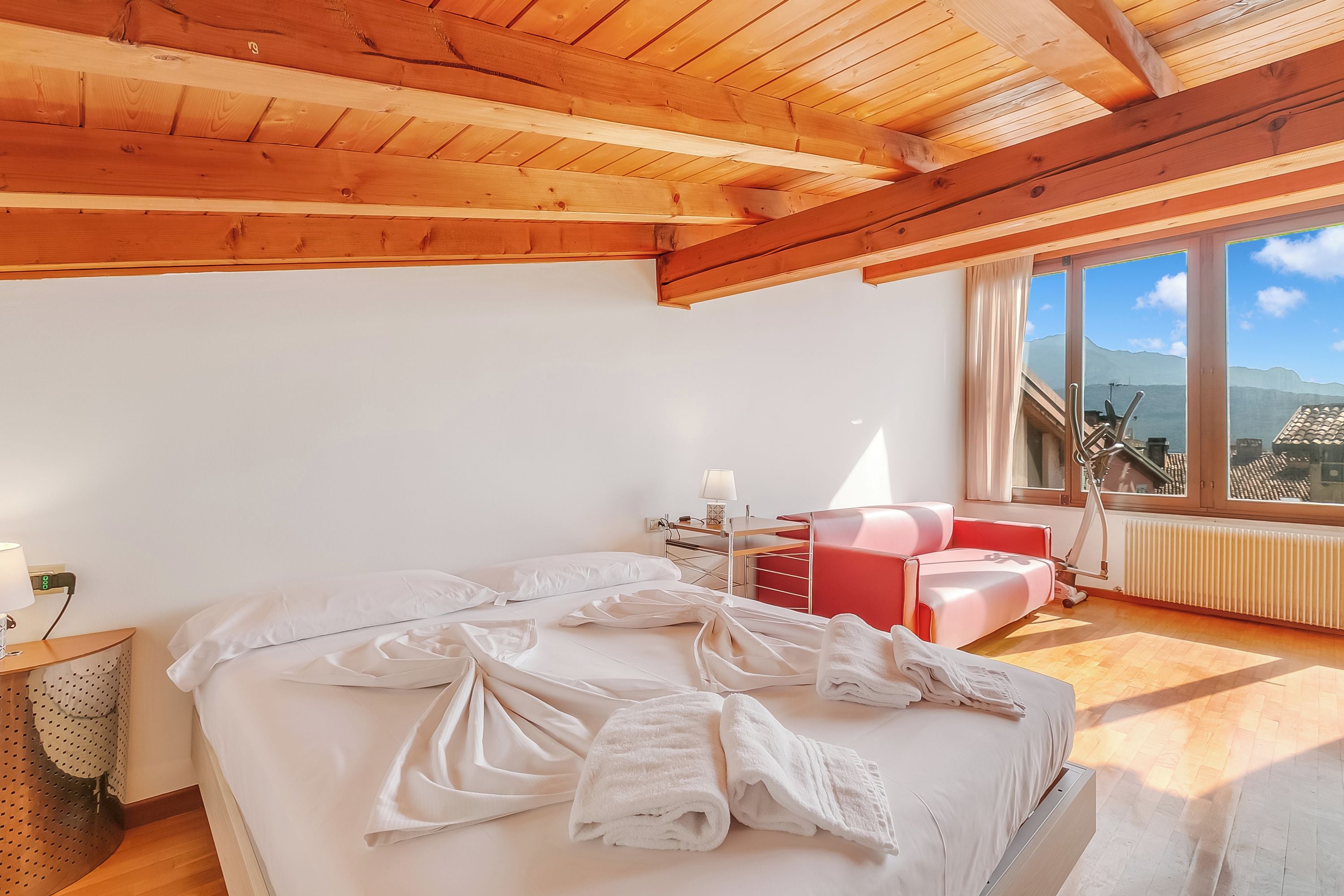 A bedroom with a large bed, a desk, a chair, and a view of the mountains through the window.